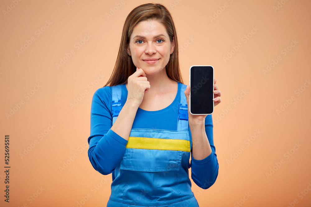 Smiling woman in overalls uniform showing smartphone screen. Isolated female worker portrait. Smiling woman in overalls uniform showing smartphone screen. Isolated female worker portrait.