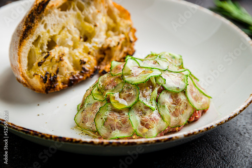Tartare from beef with sliced cucumbers on plate on dark table macro close up