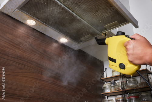 house cleaning. Girl brushes steam cleaners kitchen drawing with steam in green gloves. cleaning of a surface. photo