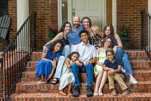 A large and blended and mixed happy family sitting on the front steps of their brick home in the suburbs photo