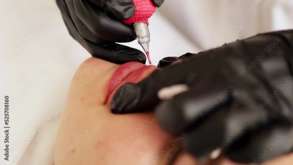 Permanent makeup procedure applying rose red pigment using tattoo machine in beautician salon. Microblading tattoo lips