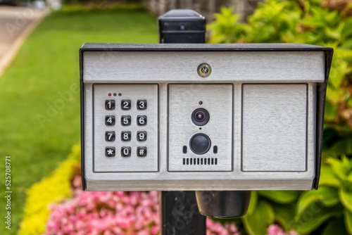 Electric key pad gate opener with camera and microphone outside estate with beautiful blurred flowers in the background
