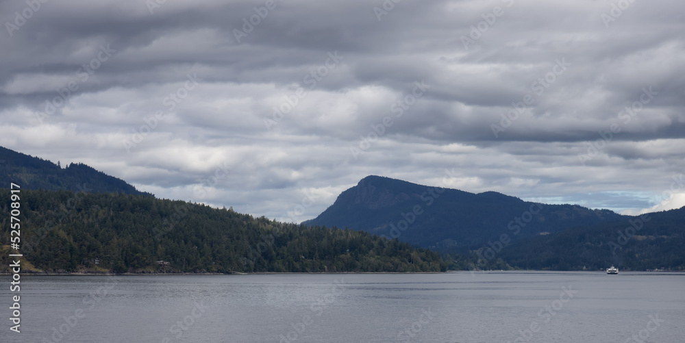 Treed Island with Homes and ferry passing by, surrounded by ocean and mountains. Summer Season. Gulf Islands near Vancouver Island, British Columbia, Canada. Canadian Landscape. Cloudy Sky