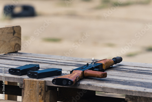 Black and brown rifle along with two clips placed on a wooden table. Outdoor shooting range competition. Firearm concept. No people. High quality photo