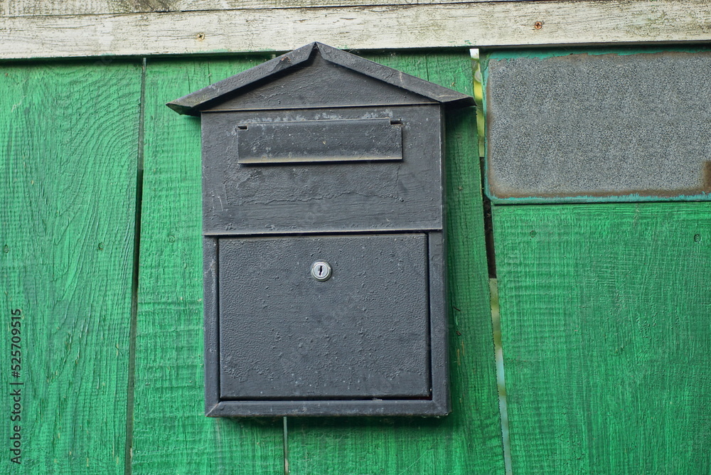 one black metal mailbox hanging on the green wooden boards of the fence wall in the street