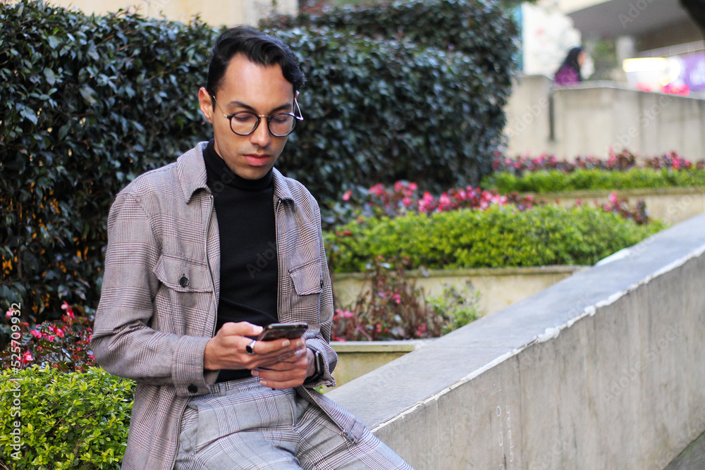 Obraz premium young man with glasses using his cell phone while sitting in a park sending a message