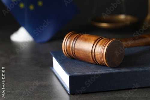 Wooden judge's gavel and book on grey table against European Union flag, closeup. Space for text