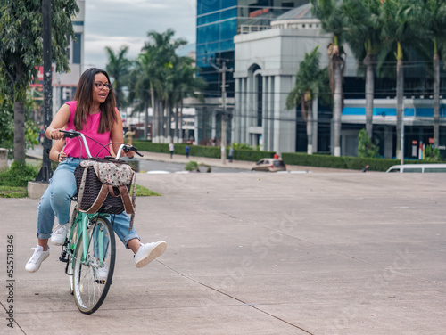 Two young Hispanic women have fun riding bicycles in the central square of El Salvador.