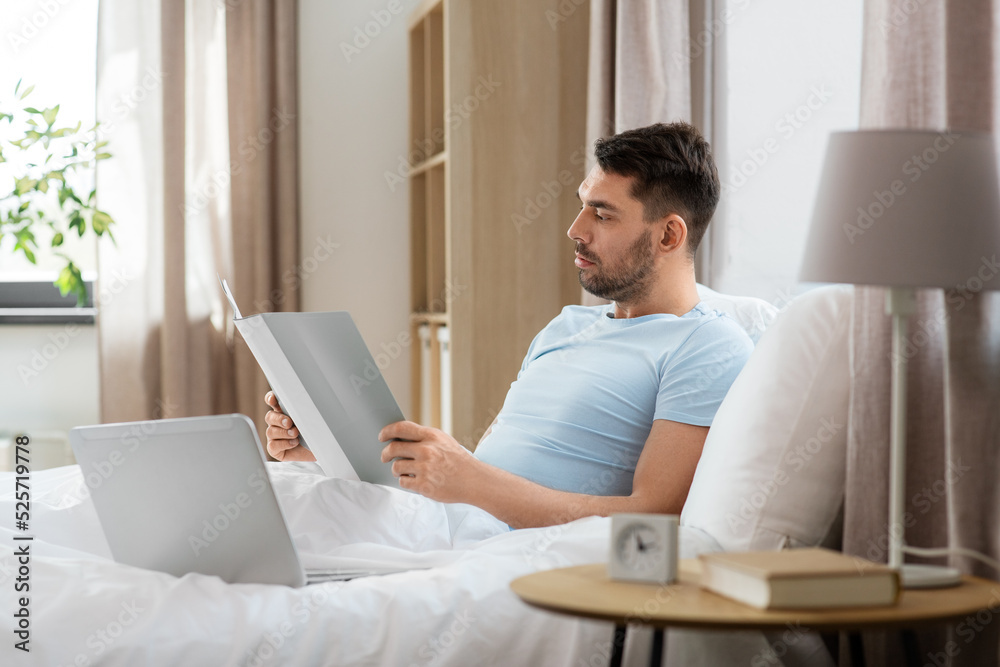 people, technology and remote job concept - man with laptop computer and folder working in bed at home bedroom people, technology and remote job concept - man with laptop computer and folder working in bed at home bedroom