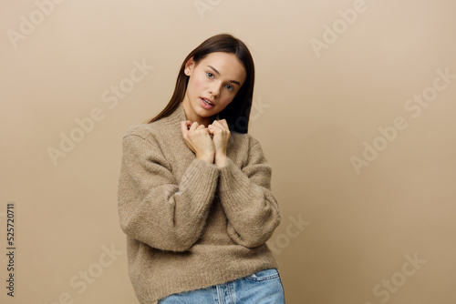 a beautiful, attractive, relaxed woman stands on a beige background in a warm, textured sweater and pulls the neck with her hands © Tatiana