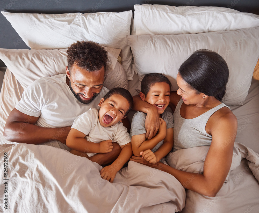 Happy family bonding in bed together, playing and laughing while being loving and having fun. Young caring interracial parents sharing special moment of parenthood with two playful boys in bedroom