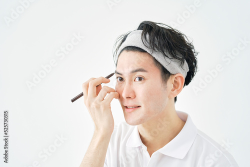 白背景でアイブロウペンシルで眉毛を描く男性