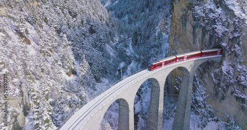 Landwasser Viaduct world heritage sight with luxury Glacier and Bernina express in Swiss Alps snow winter scenery. Aerial Drone shot red train passing through famous mountain in Filisur, Switzerland.