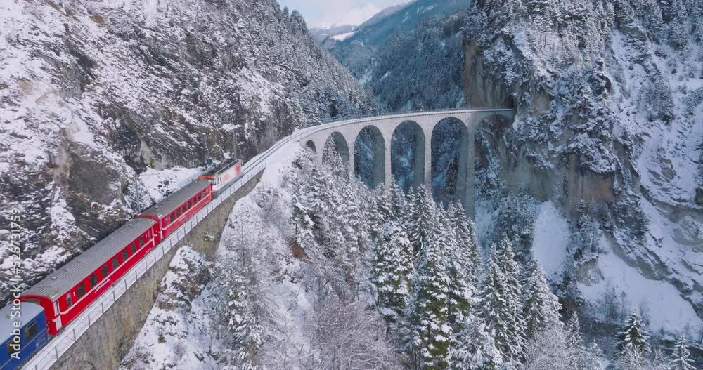 Landwasser Viaduct world heritage sight with luxury Glacier and Bernina express in Swiss Alps snow winter scenery. Aerial Drone shot red train passing through famous mountain in Filisur, Switzerland.