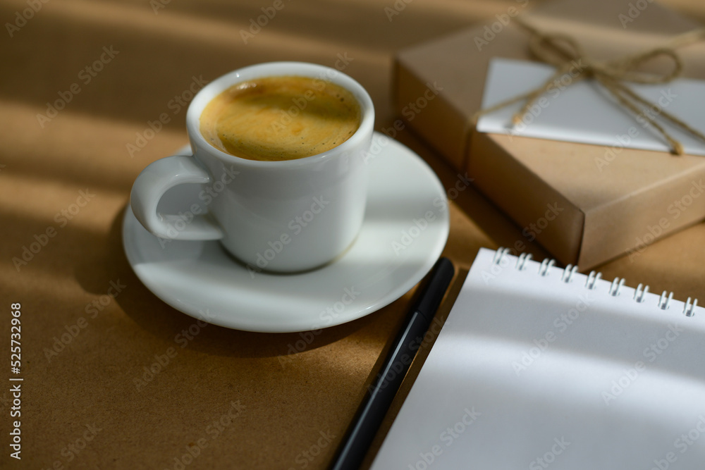 A cup of coffee on desktop. Coffee break. Coffee, notepad, workplace and gift box with blank greeting card, soft focus, blurred background A cup of coffee on desktop. Coffee break. Coffee, notepad, workplace and gift box with blank greeting card, soft focus, blurred background