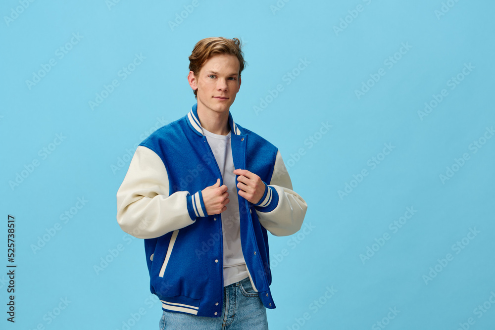 a handsome, fashionable guy in a blue bomber jacket is standing straightening his jacket on a plain background with empty space for text. studio photo a handsome, fashionable guy in a blue bomber jacket is standing straightening his jacket on a plain background with empty space for text. studio photo