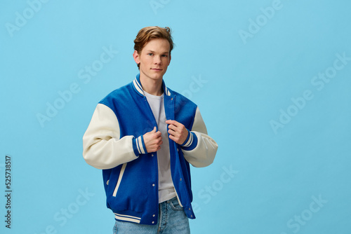 a handsome, fashionable guy in a blue bomber jacket is standing straightening his jacket on a plain background with empty space for text. studio photo