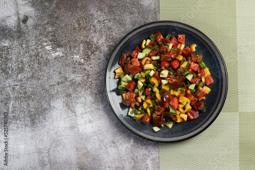 Summer homemade tomato, cucumbers and bell pepper salad in a bowl on a dark background. Top view, flat lay .