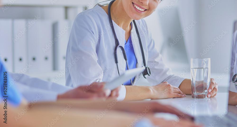 Smiling doctor using a laptop working with her colleagues in a bright hospital room Smiling doctor using a laptop working with her colleagues in a bright hospital room