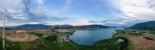 Aerial View of Okanagan Lake with farm lands and mountain landscape. Cloudy Sunset Sky. Near Vernon, British Columbia, Canada. Nature Panorama Background