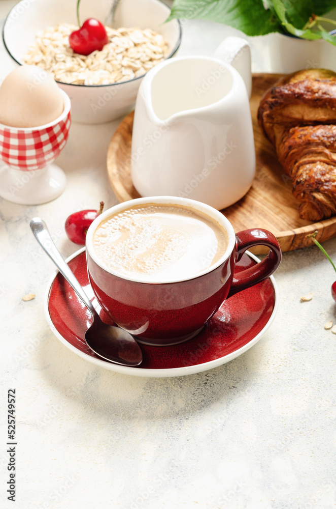 Breakfast with capuccino or caffelatte in a red cup with croissant and muesli on light background. Breakfast with capuccino or caffelatte in a red cup with croissant and muesli on light background.