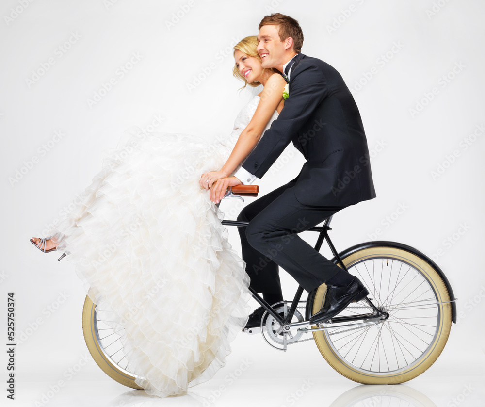 Happy, wedding and couple on a bicycle against a white background, after getting married together. Love, young bride and groom in dress and suit, cycling on a bike in marriage happiness or bliss Happy, wedding and couple on a bicycle against a white background, after getting married together. Love, young bride and groom in dress and suit, cycling on a bike in marriage happiness or bliss