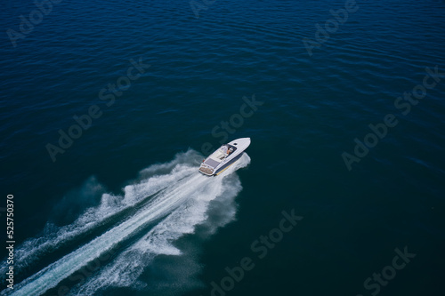 Large high speed yacht fast moving diagonal air view. A white boat with a man is moving fast on dark blue water. White blue boat in motion top view.