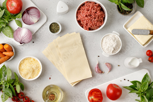 Lasagna Ingredients for making traditional italian lasagna. Uncooked Pasta, cheese, mince, oil and vegetables on gray background, top view.