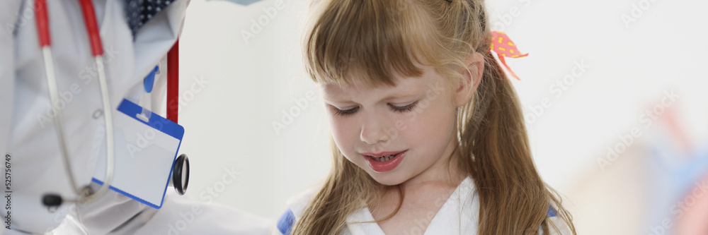 Doctor pediatrician in protective medical mask talking to little girl patient in clinic Doctor pediatrician in protective medical mask talking to little girl patient in clinic