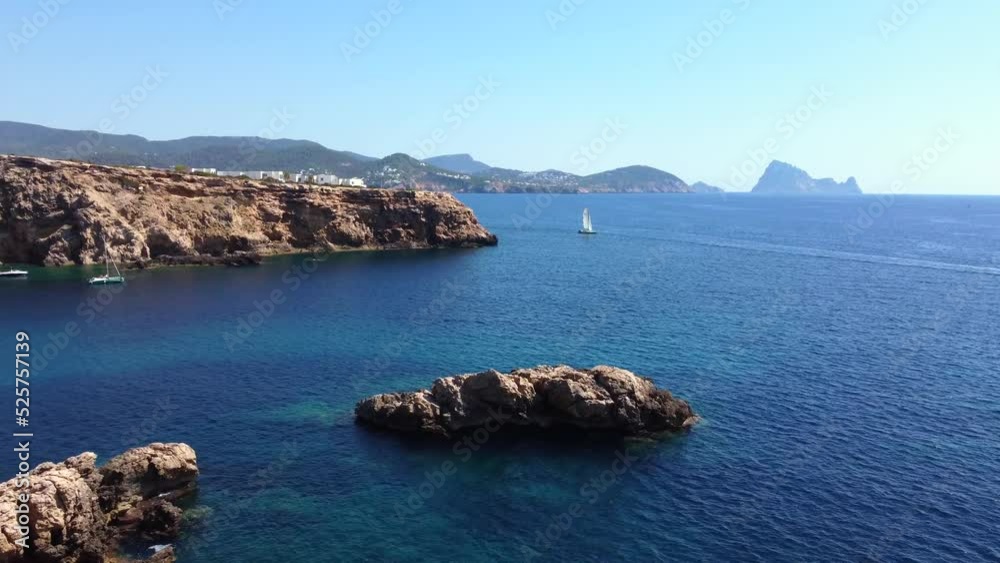 Sailing boat in the bay surrounded by cliffs.
Unbelievable aerial view flight panorama overview drone footage
of cliff edge beach Sa Figuera borda Ibiza summer 2022. P. Marnitz 4k Cinematic from above
