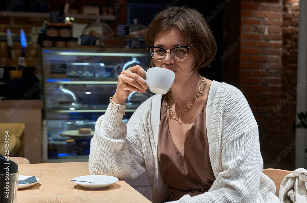 A girl in casual clothes sits in a cafe with a cup of coffee in her hands A girl in casual clothes sits in a cafe with a cup of coffee in her hands