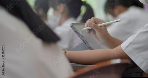 Blurred scene of Asian high school student sitting in class lecture. There is a student uses a pen to write on the tablet screen.