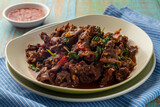 Beef pad kra pao or spicy stir-fried holy basil beef slices, served on a white-beige plate together with garlic chili relish. Pad krapao is one of popular Thai food dishes.