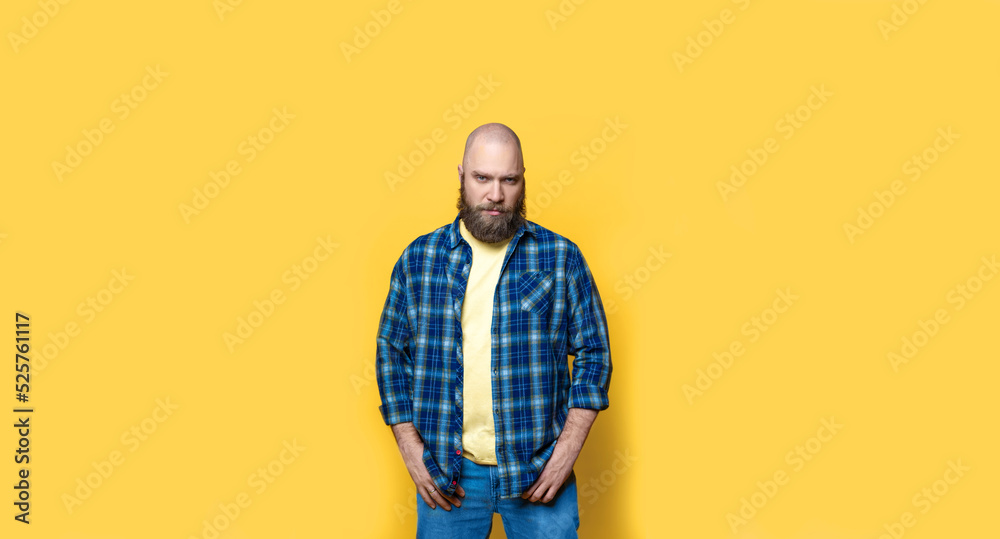 Bearded Brutal man with hands in pockets looking at camera over yellow background. Mock up, template, copy space. Confident, handsome, serious. Casual clothing, plaid blue shirt and jeans. Bearded Brutal man with hands in pockets looking at camera over yellow background. Mock up, template, copy space. Confident, handsome, serious. Casual clothing, plaid blue shirt and jeans.