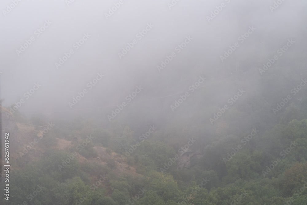 Fog view on the Khndzoresk suspension bridge in the cave city in the mountain rocks. Armenia landscape attraction. Abandoned ruins in the mist. Atmospheric stock photo.