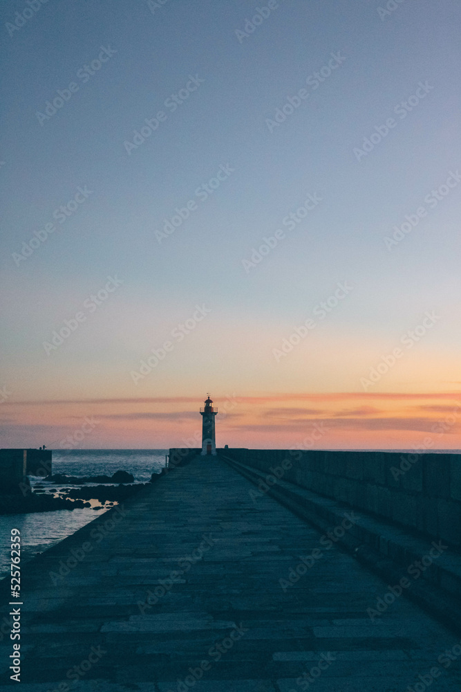 View of lighthouse at sunset with huge stones and calm water 