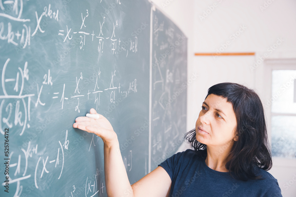 Female student or teacher in the classroom writing on chalkboard mathematical equations Female student or teacher in the classroom writing on chalkboard mathematical equations