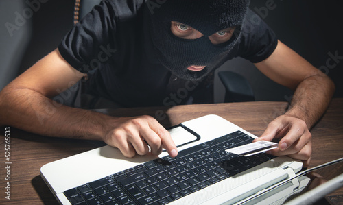 Hacker with credit card and laptop computer. Cyber crime