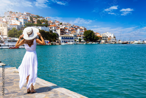 A beautiful tourist woman in a white summer dress enjoys the view to the city of Skopelos island, Sporades, Greece