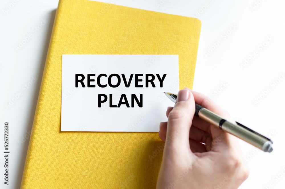 RECOVERY PLAN text is written with a pen by a doctor on a card that lies on a yellow closed notebook on a light background, medical concept RECOVERY PLAN text is written with a pen by a doctor on a card that lies on a yellow closed notebook on a light background, medical concept