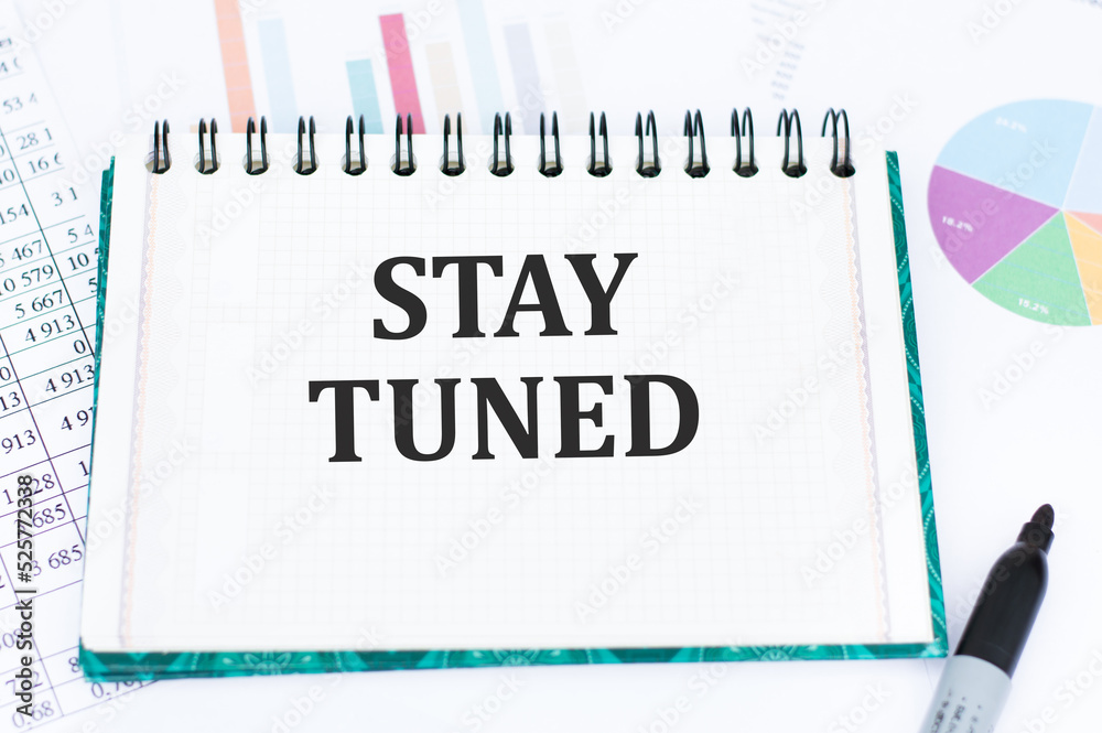 a white notebook with the words STAY TUNED and a pen. a white notebook with the words STAY TUNED and a pen.