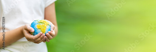 Little girl holding small planet in hands against spring or summer green background. Horizontal banner for web design with copy space.Ecology, environment and Earth day concept. 