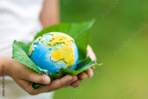 Fototapeta Naklejka Na Ścianę i Meble -  Kid holding small planet in hands against spring or summer green background. Ecology, environment and Earth day concept. 