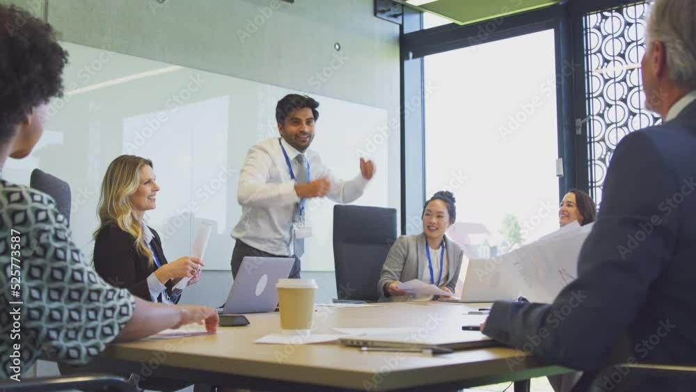 Multi-cultural business team throwing paperwork in the air after businessman announces successful deal during meeting around boardroom table - shot in slow motion Multi-cultural business team throwing paperwork in the air after businessman announces successful deal during meeting around boardroom table - shot in slow motion