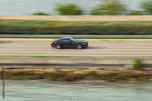 A sleek racing car speeds down the road in a thrilling side-view shot, capturing its power, motion, and aerodynamic precision in an intense high-speed action moment.