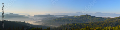 Sunrise in Carpathian mountains. Silhouettes of mountain peaks and morning fog. Dense forest in the foreground.