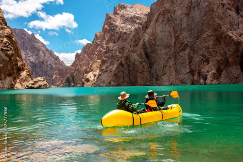 Kayaking on a mountain lake. Two men are sailing on a yellow canoe along the lake along the rocks. The theme of water sports and summer holidays.