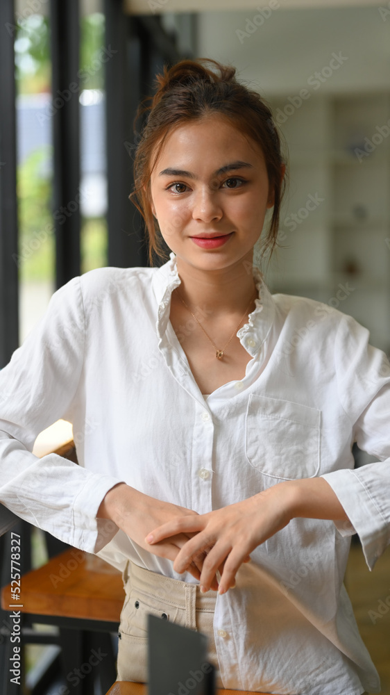 Portrait of beautiful young female office worker in white shirt sitting in bright office and looking at camera Portrait of beautiful young female office worker in white shirt sitting in bright office and looking at camera
