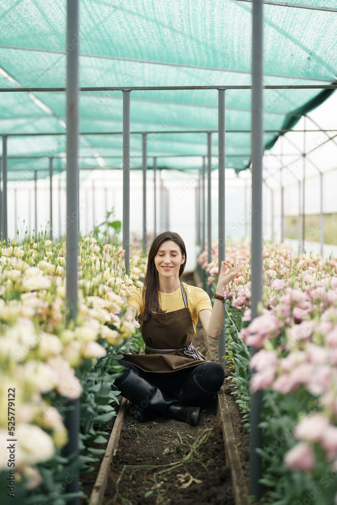 Pretty women relaxing among flowers while sitting in a meditation pose in the green house