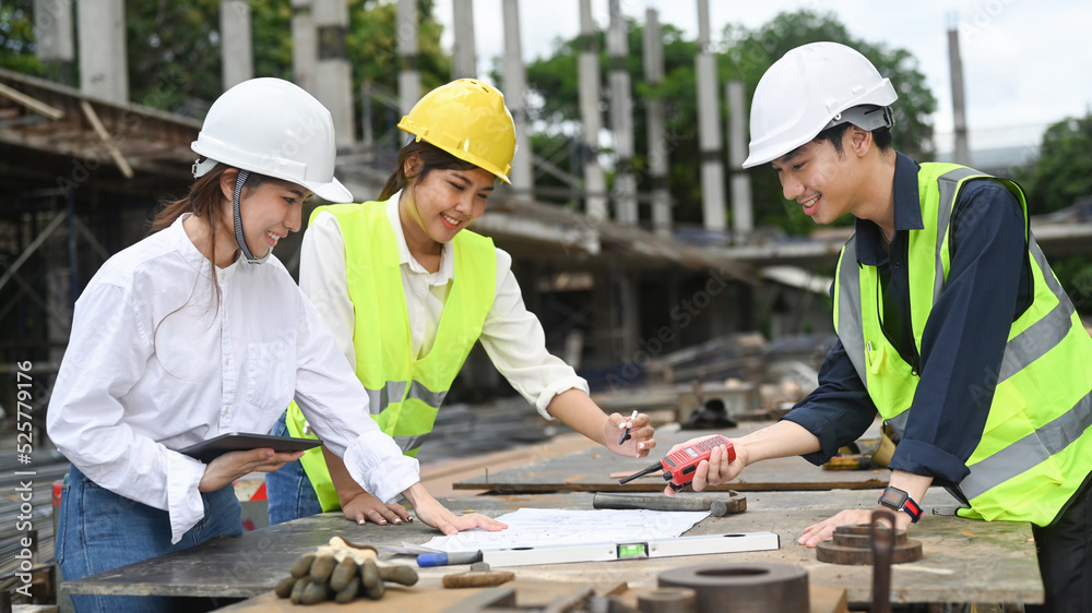 Engineer or architect and real estate investor wearing safety helmets examining plans and discussing the construction process together Engineer or architect and real estate investor wearing safety helmets examining plans and discussing the construction process together